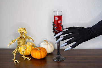 Witch hand with long silver nails take glass of vine with eyeballs from the table. Scary drink....