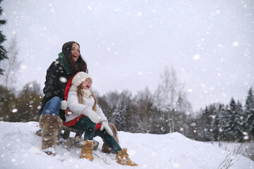 A winter fairy tale, a young mother and her daughter ride a sled in the forest. A girl on a sled with gifts on the eve of the new year in the park. 