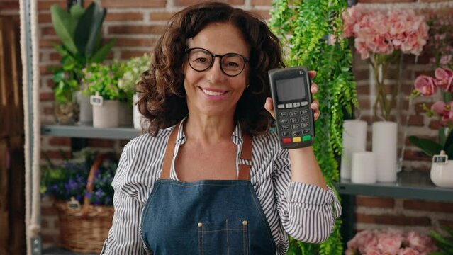 Middle age woman florist smiling confident holding data phone at flower shop