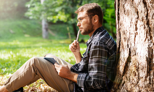 Man planning his business, thinking and writing his ideas in his notebook, male person touching lips with a pen.
