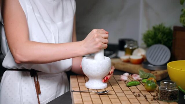 Stone grinding bowl on wooden board for crushing spices and herbs, woman mixing aroma flavours in stone mortar with pestle in the kitchen, preparation of aroma powder for meat, fish or vegetables