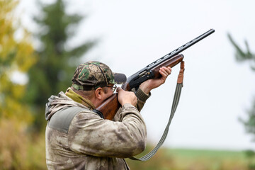 The hunter aims at the target - prey from a hunting gun in the forest in light rain. A hunter with a gun in his hands at the opening of the hunting season.Shooting with weapons on the hunt.