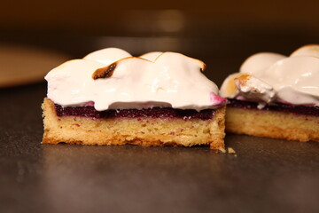 Tart slice with meringue on a dark background. Side view. Professional dessert. Jam filling, jam inside the tart. Closeup cut, slice.