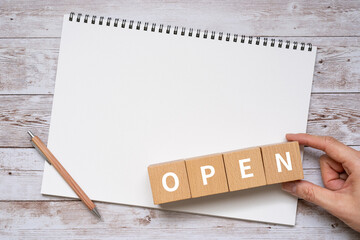 OPENと書かれたブロック、ノート、ペン、手
