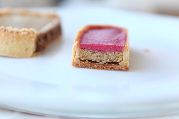 Tart slice with meringue on a dark background. Side view. Professional dessert. Jam and raspberry cream filling, jam  and pistachios inside the tart. Closeup cut, slice.