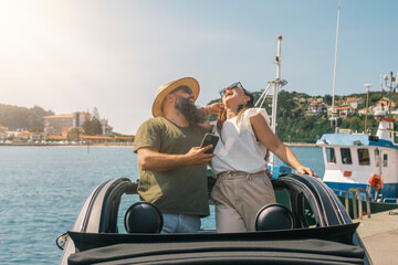 pareja riéndose en un coche descapotable junto a un puerto pesquero