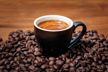 Kawa espresso w czarnej filiżance  na drewnianym stole pełnym świeżo palonych ziaren kawy - obrazy, fototapety, plakaty