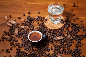 Czarna kawa espresso w czarnej filiżance i szklanka wody  na stole pełnym świeżo palonych ziaren kawy - obrazy, fototapety, plakaty