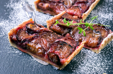 Traditional German zwetschgenkuchen with sliced plums and icing sugar served as close-up on a black board