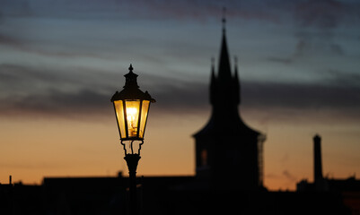Fototapeta na wymiar Vintage street light in foreground of an amazing silhouette landscape with Prague architecture next to Charles Bridge and Old Town clock in background. Travel to Czech Republic.