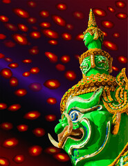 Side view of a giant Tosakan with 10 faces and 10 arms, green body, The background has a red light.