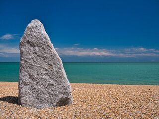 A tall, 2m, grey standing stone on the shingle beach at Walmer, Deal, Kent, UK. Taken on a sunny...