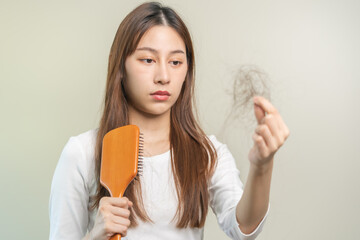 Serious, worried asian young woman, girl holding brush, show her comb, hairbrush with long loss hair problem after brushing, hair fall out on her hand in living room. Health care, beauty treatment.