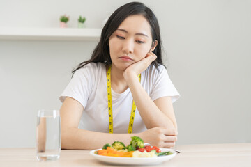 Obraz na płótnie Canvas Diet in bored face, unhappy beautiful asian young woman on dieting, looking at salad plate on table, dislike or tired with eat fresh vegetables. Nutritionist of healthy, nutrition of weight loss.