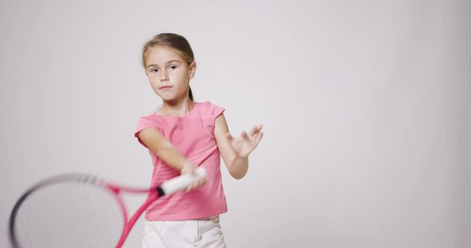 Young female tennis player. Girl in pink sports outfit practicing forehand and backhand movement.