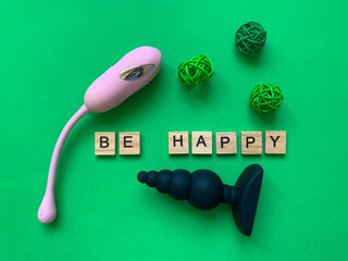 Two sex toys on green background. Lettering BE HAPPY. Assortment sex shop