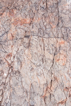 Beautiful relief vertical texture of the surface made of natural clay or stone with many long branched cracks of brown, orange and gray colors