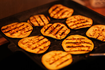 Homemade autumn vegetables recipes. Detail view with round slice cuts of eggplant on a grill inside an apartment kitchen.