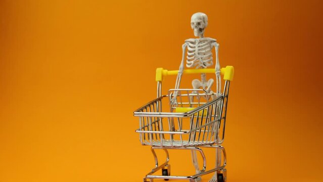 a skeleton is driving a cart from a supermarket on an orange background, the concept of shopping sales in honor of the Halloween holiday