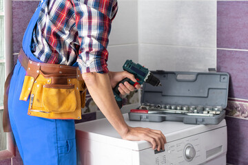 working man plumber repairs a washing machine in laundry