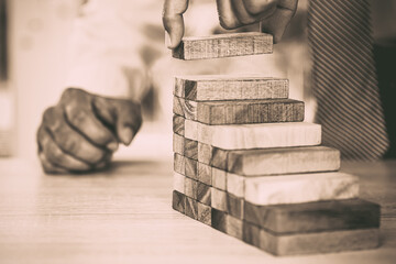 Hand placing wooden block tower stack in pyramid stair step with caution to prevent collapse or...