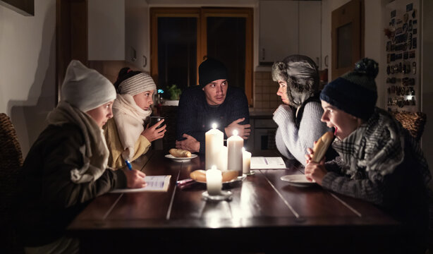 Worried parents discuss their stressing situation of no heat and light due to energy crisis at the table while kids try to eat and study by the lights of candles
