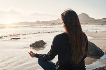 silhouette of a person sitting meditating on the rock on the coast at sunset back view