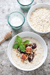 Bowl of oatmeal with figs, date fruits and honey, high angle view on a light-brown granite background, vertical shot