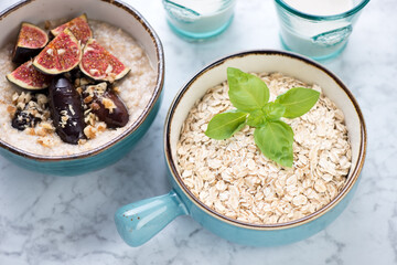 Turquoise bowls with oat flakes and oatmeal with dates and figs, horizontal shot on a light-grey marble background