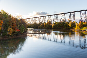 Fototapeta na wymiar View of the 1908 railway trestle bridge and its reflection in the Cap-Rouge River seen during a fall morning golden hour, Quebec City, Quebec, Canada