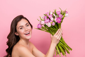 Obraz na płótnie Canvas Photo of charming excited young nude lady wear nothing holding tulips bloom isolated pink color background