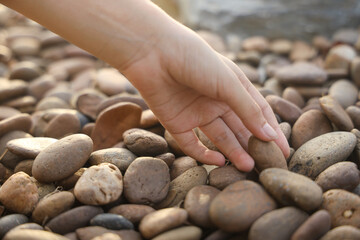 female hand holding small pebble stones picking up pebbles, round shape pebbles, summer vacation...