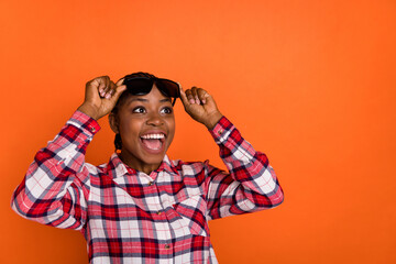 Portrait of astonished girl arms touch glasses look empty space isolated on orange color background