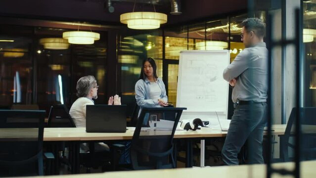Creative asian woman presenting blueprint on flipchart or engineering startup project to colleagues in modern office. Business meeting in office conference room. Discussion about new technologies.