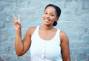Portrait, peace sign and happy black woman with wall background smiling and standing proud and...
