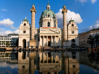 Fototapeta premium Vienna, Austria - July 6 2022: High resolution image of Karlskirche reflected in the water at Karlsplatz. Summer day at marvelous Karlskirche in Vienna, big pillars of marble reflected in the water