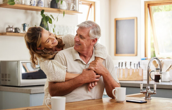 Senior couple, hug and bonding with morning coffee in a house or home kitchen in trust, security and love. Smile, happy and retirement elderly man and mature woman with tea and safety life insurance
