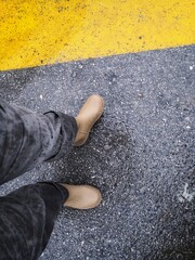 feet on the pavement, rainy season, rubber shoes, light brown rubber boots in water on asphalt road.
