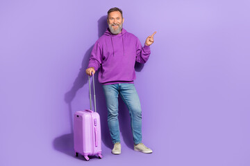 Full size photo of cheerful positive retired man wear purple sweatshirt jeans directing empty space isolated on violet color background