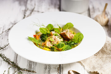 Salmon cutlet with fish broth and vegetables. Appetizing fish meatballs. Served on a white plate. Wooden white background. Close-up