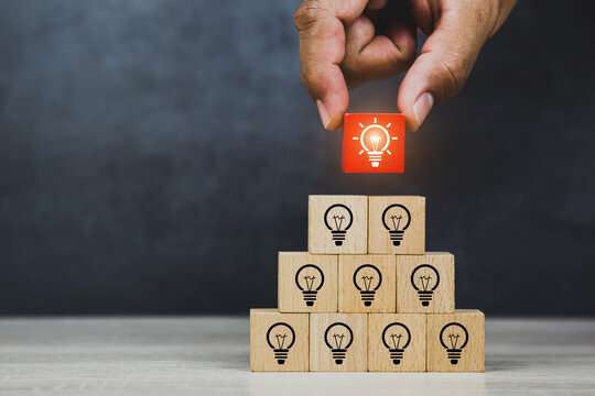 Hand choose bright light bulb on wooden block stack pyramid for human resources or leadership and creativity thinking idea motivation or vision and knowledge learning and study or education concept.