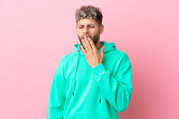 Young handsome caucasian man isolated on pink background yawning and covering wide open mouth with hand