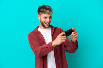 Young handsome caucasian man isolated on blue background playing with the mobile phone