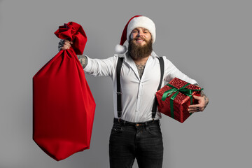 Christmas bearded smiling man in white shirt holds sack and gift box in his hand. New Year