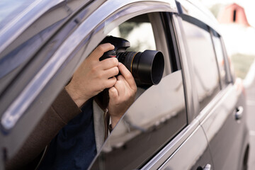 Private detective or investigator or paparazzi taking photos on street while sitting in car