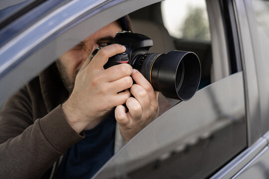 Investigator or private detective, reporter or paparazzi sitting in car and taking photo with professional camera