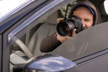 private detective sitting inside car taking picture with professional slr camera - obrazy, fototapety, plakaty