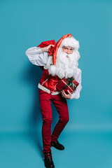Full size of slinking santa who claus carrying huge bag of presents while holding gift box in hand