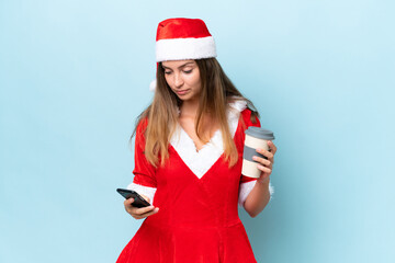 Young caucasian woman dressed as mama noel isolated on blue background holding coffee to take away and a mobile