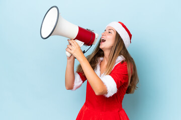 Young caucasian woman dressed as mama noel isolated on blue background shouting through a megaphone